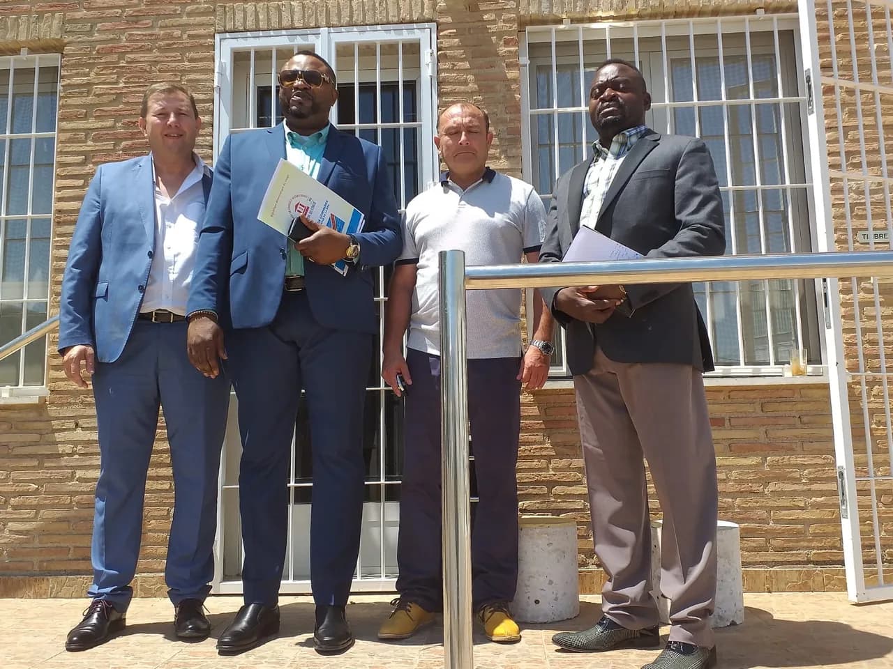 Quatre hommes en tenue professionnelle debout devant un bâtiment en briques, tenant des documents, lors d'une rencontre de travail en Espagne.